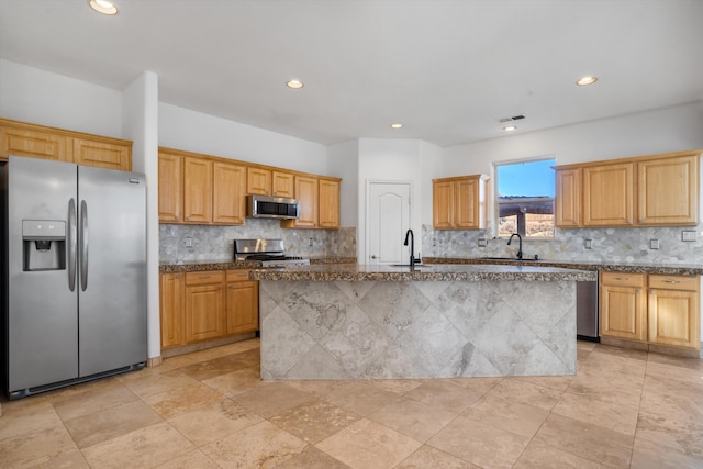 kitchen featuring stainless steel appliances, an island with sink, stone counters, and decorative backsplash