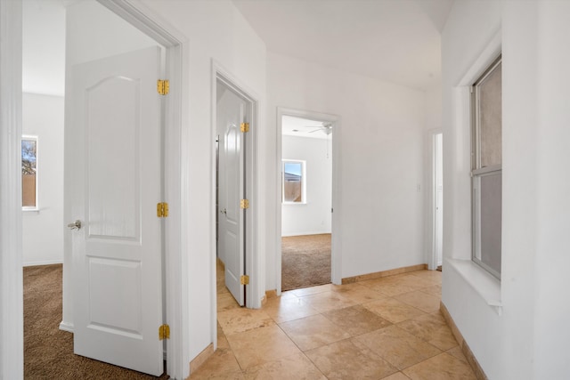 corridor featuring light colored carpet and baseboards