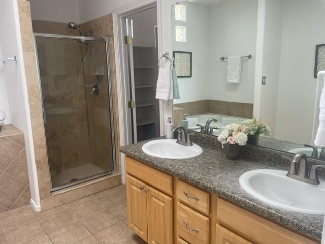 bathroom with tile patterned flooring, a stall shower, double vanity, and a tub