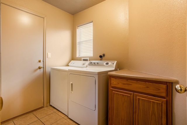 clothes washing area with washer and clothes dryer, light tile patterned floors, cabinets, and a textured ceiling