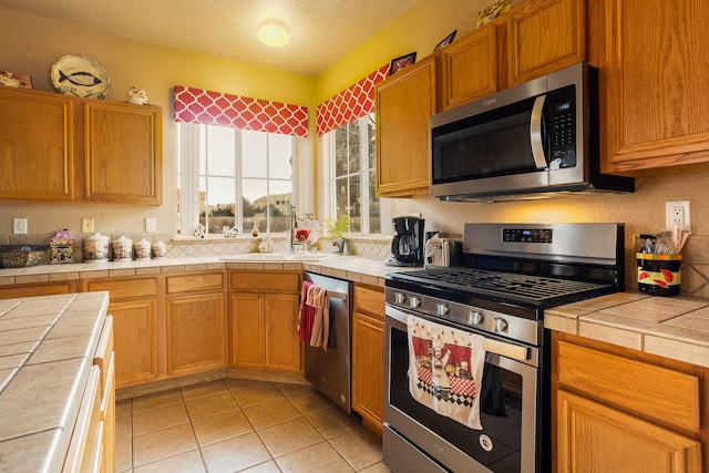 kitchen featuring tile countertops, sink, light tile patterned floors, and appliances with stainless steel finishes