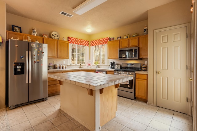 kitchen featuring a breakfast bar, light tile patterned floors, appliances with stainless steel finishes, tile counters, and a kitchen island