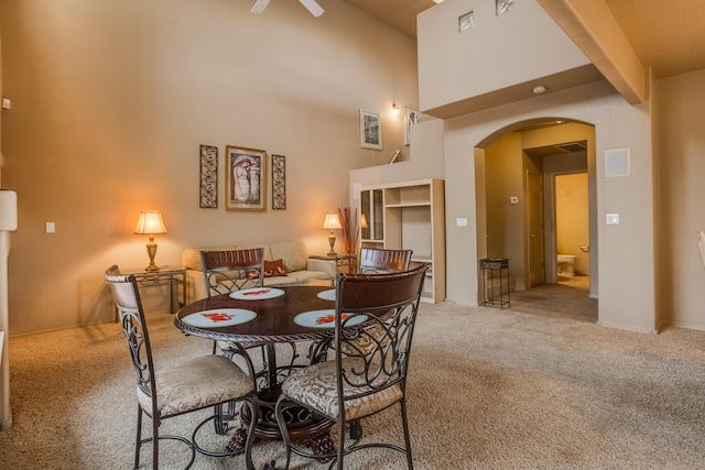 carpeted dining room featuring ceiling fan, beamed ceiling, and a towering ceiling