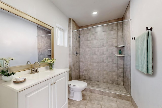 bathroom with toilet, a tile shower, vanity, and tile patterned flooring