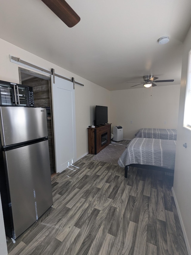 bedroom with dark hardwood / wood-style floors, stainless steel refrigerator, ceiling fan, and a barn door