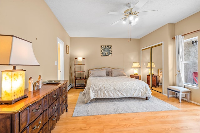 bedroom featuring multiple windows, a closet, light wood-type flooring, and baseboard heating