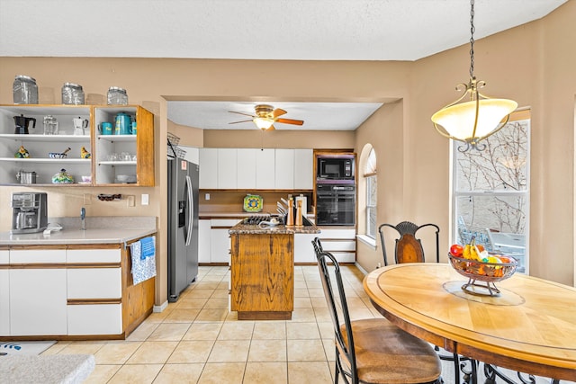 kitchen with light tile patterned floors, hanging light fixtures, black appliances, white cabinets, and a kitchen island