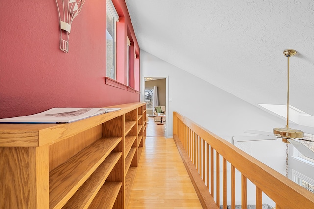 corridor featuring lofted ceiling, light hardwood / wood-style flooring, and a textured ceiling