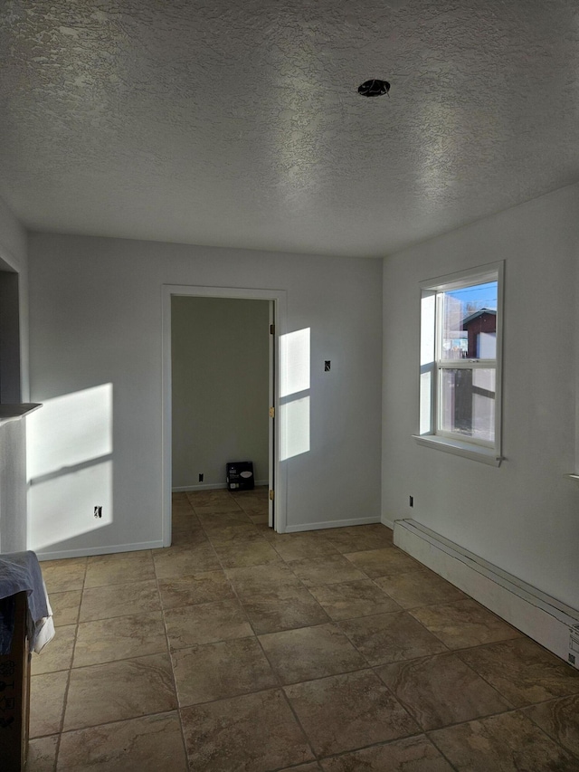 spare room featuring a textured ceiling, a baseboard radiator, and baseboards