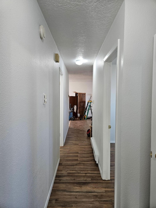 hallway with baseboards, a textured wall, dark wood-type flooring, a textured ceiling, and a baseboard heating unit