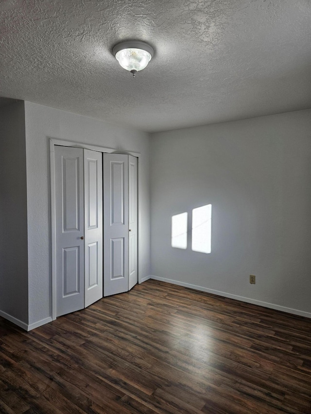 unfurnished bedroom with a closet, dark wood finished floors, a textured ceiling, and baseboards