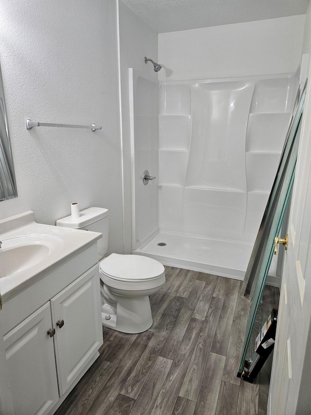 bathroom with walk in shower, vanity, toilet, and wood finished floors