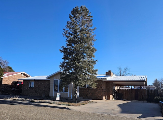 view of front of property with a chimney, fence, metal roof, a carport, and driveway