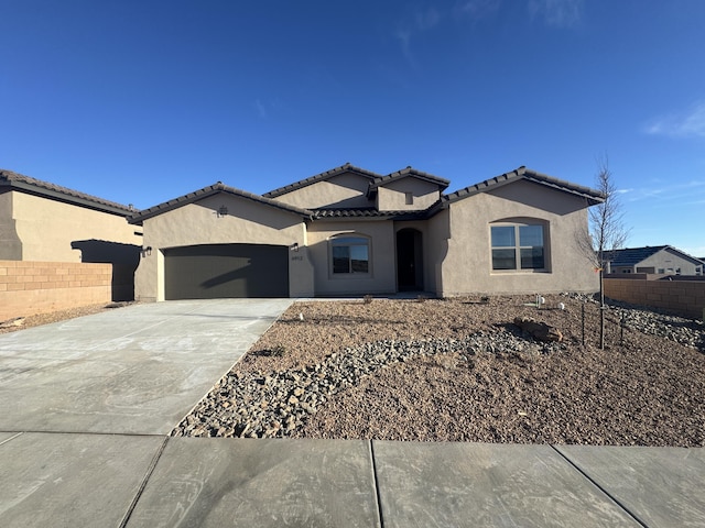 mediterranean / spanish-style home with a garage, fence, concrete driveway, and stucco siding