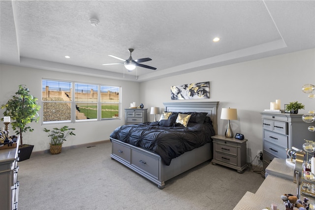 bedroom featuring light colored carpet, ceiling fan, a tray ceiling, and a textured ceiling