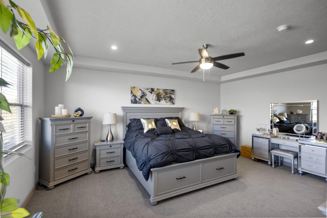 carpeted bedroom with ceiling fan, multiple windows, a textured ceiling, and a tray ceiling