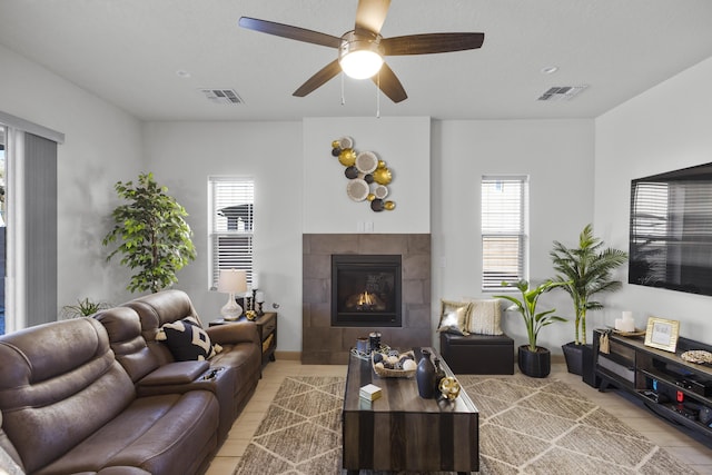 living room featuring ceiling fan, a tiled fireplace, and visible vents