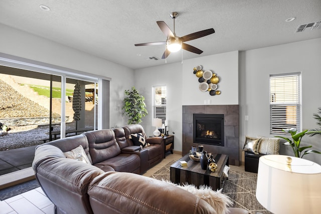 living room with visible vents, a fireplace, a textured ceiling, and ceiling fan