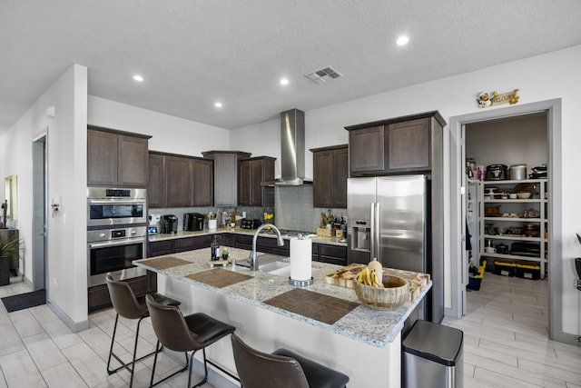 kitchen featuring wall chimney exhaust hood, a kitchen breakfast bar, dark brown cabinets, visible vents, and stainless steel appliances