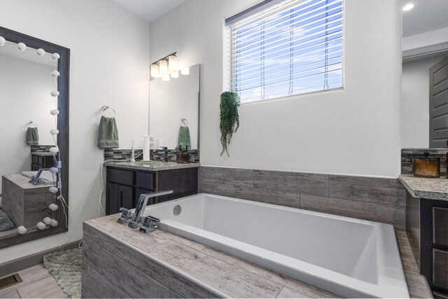 bathroom with tiled bath and vanity