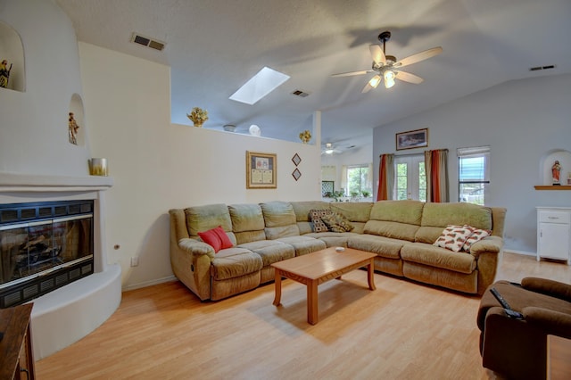 living room with ceiling fan, vaulted ceiling with skylight, and light hardwood / wood-style floors