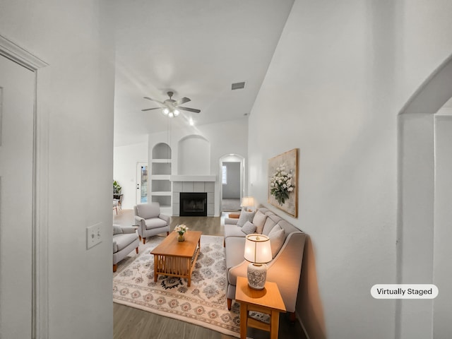 living room featuring ceiling fan, a fireplace, built in features, and hardwood / wood-style flooring