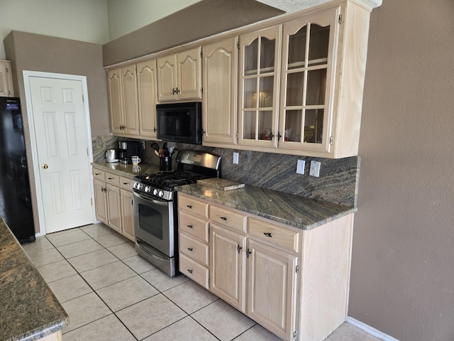 kitchen featuring light brown cabinetry, tasteful backsplash, light tile patterned floors, dark stone countertops, and black appliances