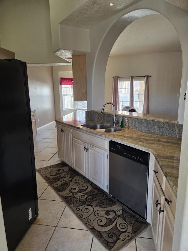 kitchen featuring sink, light tile patterned flooring, stainless steel dishwasher, and black fridge