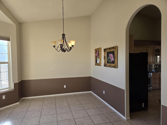 empty room with lofted ceiling, a notable chandelier, and light tile patterned flooring