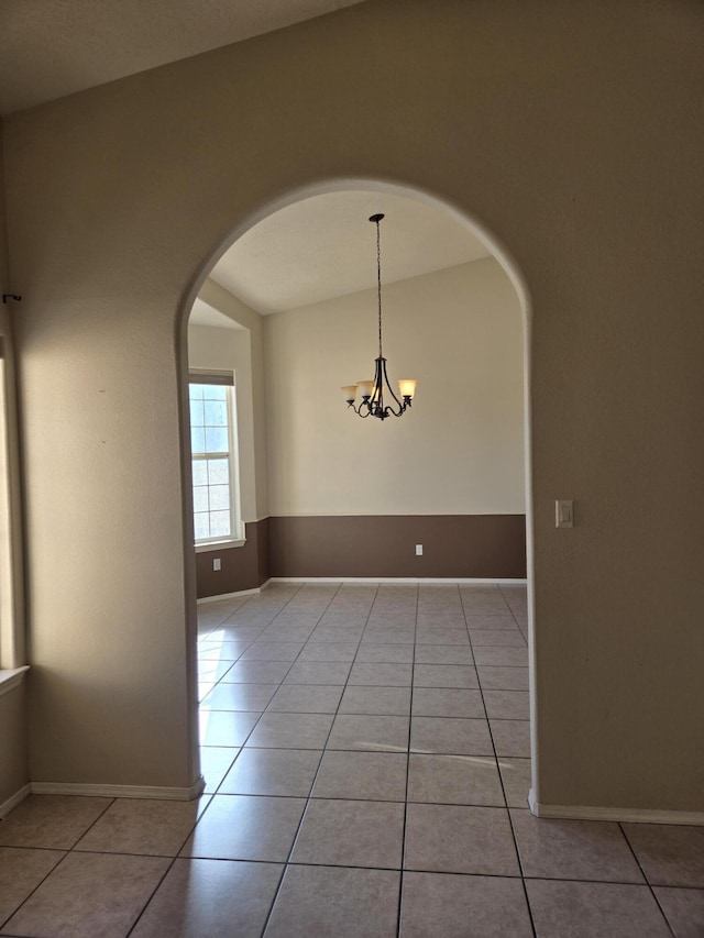 tiled spare room featuring vaulted ceiling and a notable chandelier