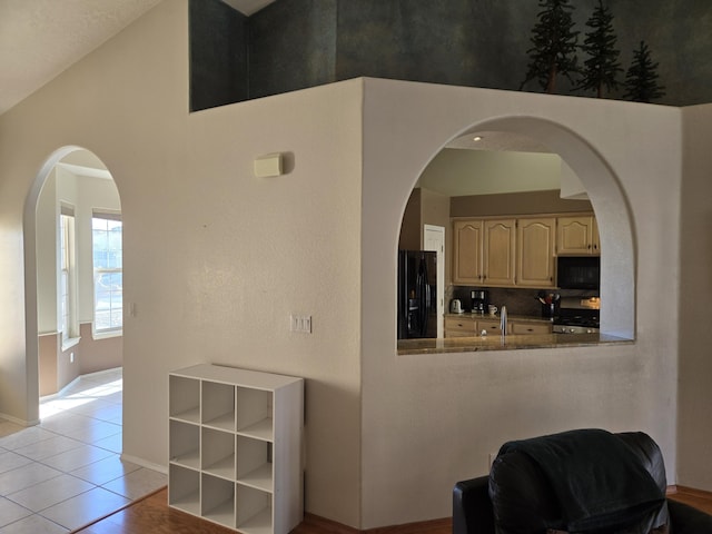 interior space with sink, black fridge with ice dispenser, vaulted ceiling, stainless steel range, and light tile patterned flooring