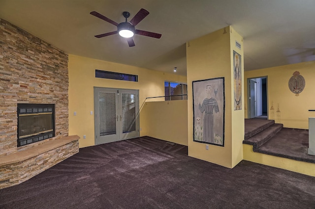 living room featuring ceiling fan, dark carpet, a stone fireplace, and french doors