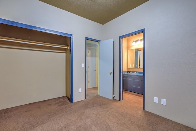 unfurnished bedroom featuring light carpet, a closet, connected bathroom, and a textured ceiling