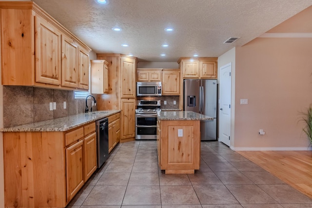 kitchen featuring appliances with stainless steel finishes, light stone countertops, a center island, backsplash, and sink