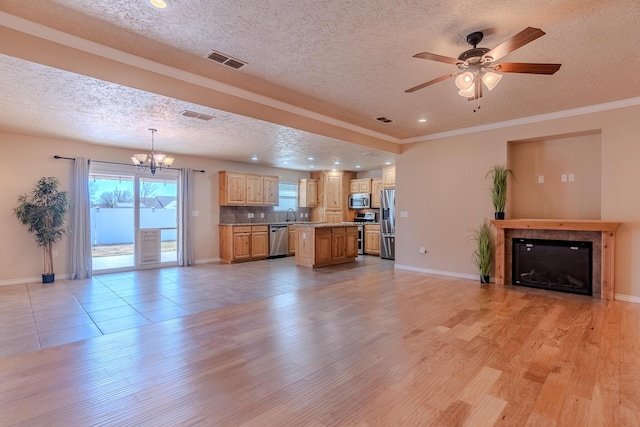 unfurnished living room featuring a tile fireplace, light hardwood / wood-style floors, sink, crown molding, and ceiling fan with notable chandelier