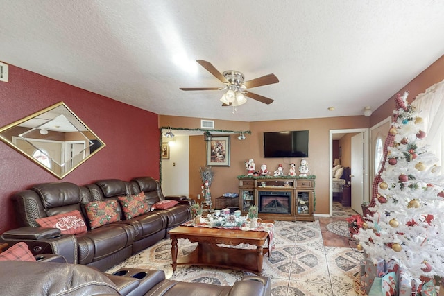 living room featuring a fireplace, a textured ceiling, and ceiling fan