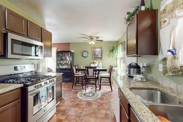 kitchen with ceiling fan, light stone countertops, a textured ceiling, light tile patterned flooring, and stainless steel appliances