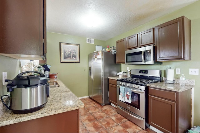 kitchen featuring light stone countertops, light tile patterned floors, stainless steel appliances, and a textured ceiling