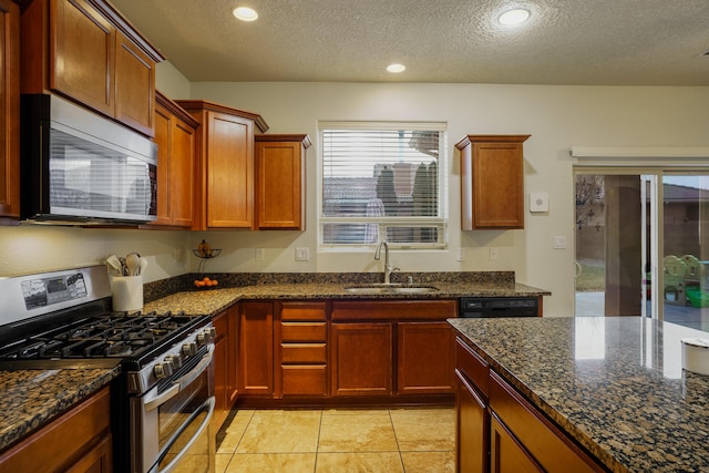 kitchen featuring sink, stainless steel appliances, dark stone counters, a textured ceiling, and light tile patterned floors