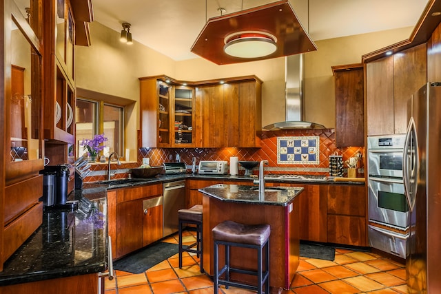 kitchen featuring sink, wall chimney exhaust hood, a kitchen island with sink, decorative backsplash, and appliances with stainless steel finishes