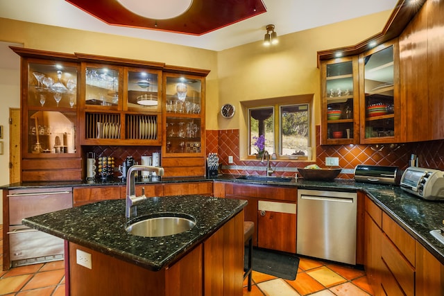 kitchen featuring dishwasher, sink, backsplash, and an island with sink