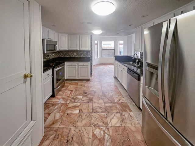 kitchen featuring stainless steel appliances, a textured ceiling, decorative backsplash, sink, and white cabinetry