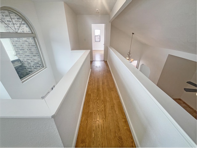 hallway with vaulted ceiling, a chandelier, and hardwood / wood-style floors