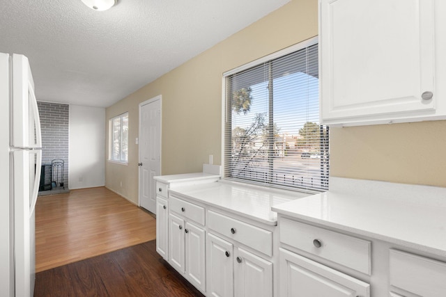 kitchen featuring white refrigerator, white cabinetry, a textured ceiling, a fireplace, and dark hardwood / wood-style floors