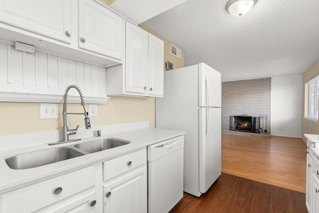 kitchen featuring sink, white appliances, white cabinetry, and a brick fireplace