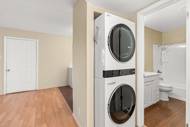 laundry room featuring a textured ceiling, light hardwood / wood-style floors, and stacked washer / dryer