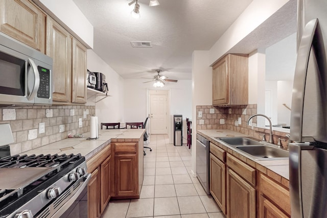 kitchen featuring appliances with stainless steel finishes, sink, backsplash, tile counters, and light tile patterned floors