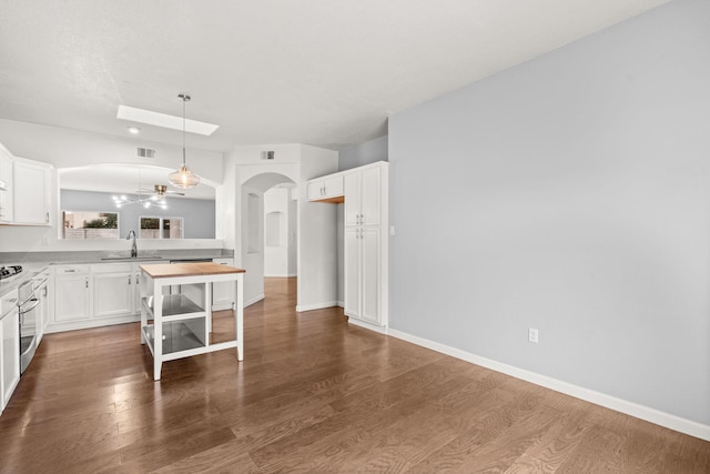 kitchen with arched walkways, dark wood-type flooring, a sink, stainless steel oven, and white cabinets