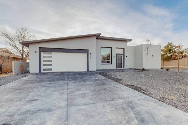 view of front of property featuring stucco siding, a garage, concrete driveway, and fence