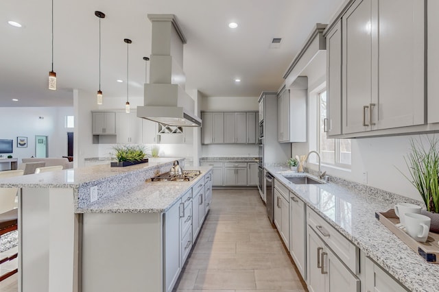 kitchen with a spacious island, light stone counters, appliances with stainless steel finishes, island exhaust hood, and a sink